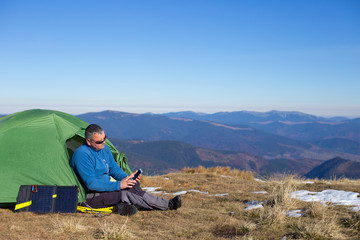 Fototapeta premium The solar panel attached to the tent. The man sitting next to mobile phone charges from the sun.