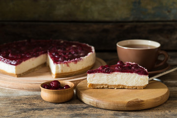 Slice of cheesecake with cherry and cup of tea on wooden background