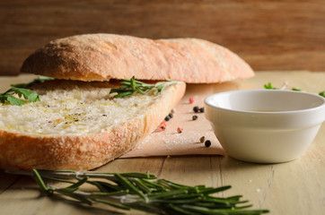 Sliced bread ciabatta watered with extra virgin olive oil with herbs  on wooden background