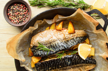 Baked fish mackerel with baked potato in a pan, rosemary, lemon and spice on a wooden background