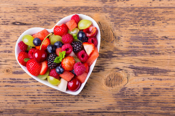 Delicious fruit salad in heart shaped bowl on wooden background