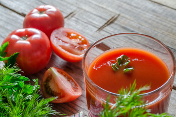 Tomato juice in glass and fresh tomatoes on rustic wooden background