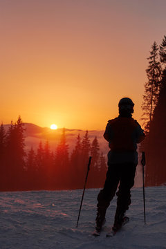 Skier silhouette high in mountains. Skier standing on a hill high above the clouds during a sunset, beautiful colorful sky with clouds in front of him.