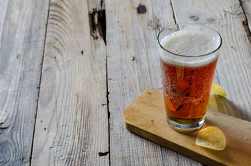 Beer into glass on wooden table with potato chips