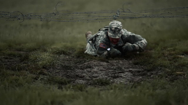 Soldier crawling under low barbed wire at an obstacle course.