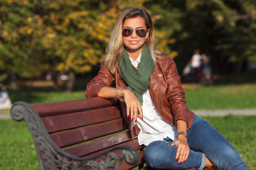 Beautiful young blond woman sitting on a bench in a park