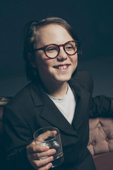 Smiling teenage boy in suit with glasses sitting on couch holdin