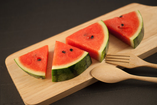 water melon slice on wood plate with fork and spoon isolated on black background