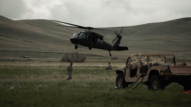 Helicopter landing in field with surrounding Humvee and soldiers