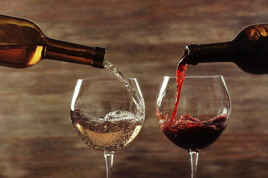 White and red wine pouring in glasses on wooden background