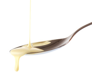 Condensed milk pouring from a spoon, isolated on white