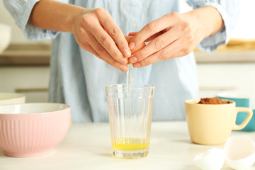 Woman is breaking an egg into a glass