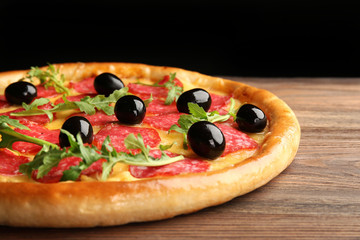 Tasty pizza with salami and olives on wooden table against black background
