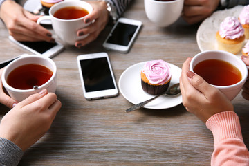 Four hands with smart phones holding  cups with tea, on wooden table background