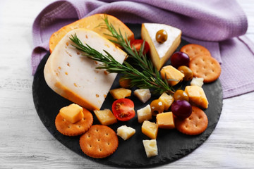 Round board with cheese, vegetables and rosemary on wooden table
