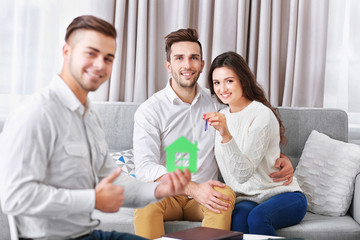 Estate agent with model of house and happy couple on home interior background