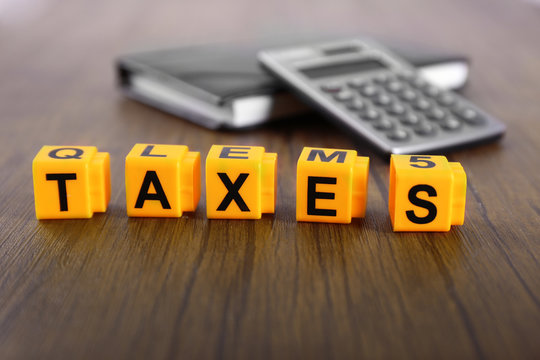 Alphabet TAXES and calculator with notebook on wooden table