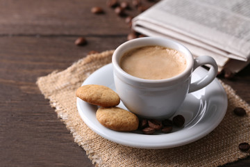 Cup of coffee, cookie and newspaper on wooden table background