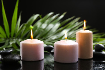 Fototapeta na wymiar Aroma candles and pebbles with palm leaves on dark background