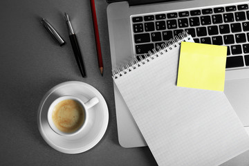 Empty yellow adhesive paper on laptop keyboard, pen and coffee cup on desk background