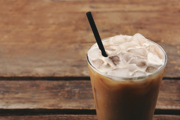 Cup of ice coffee with straw on wooden background