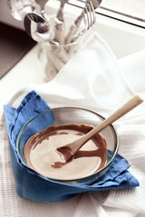 Melted chocolate in glass bowl, on wooden background