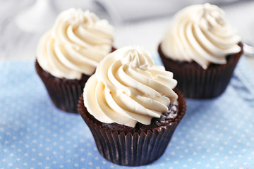 Delicious chocolate cupcakes with cream on served table, close up