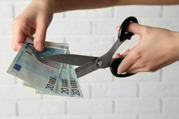 Hands with scissors cutting money on white brick wall background