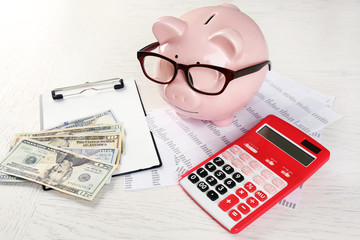 Bookkeeping concept. Piggy bank, calculator, dollars and papers on white wooden background