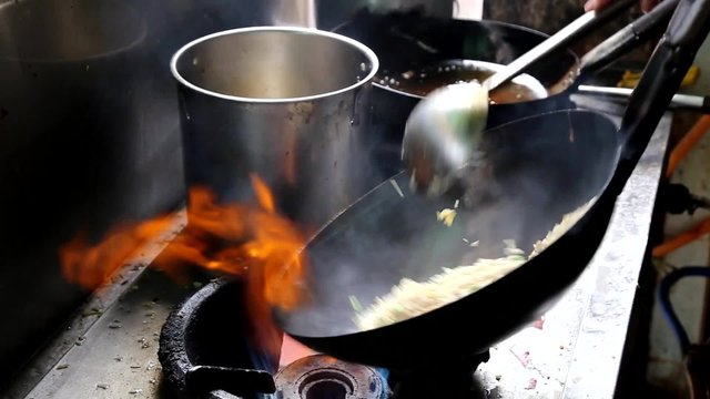 Asian chef tossing and frying rice in wok on stove with intense heat and high temperature 