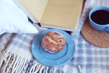 Open book, plaid and coffee on sofa. Top view