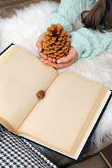 Woman holding pine cone near book with acorn, closeup