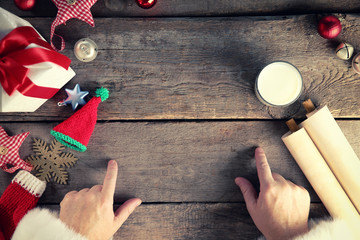 Christmas concept. Santa Claus hands, gift box, toys, glass of milk on wooden table, close up