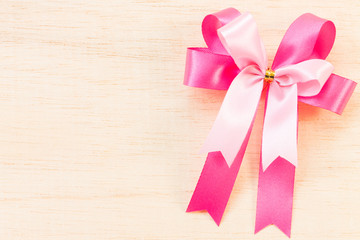 Pink ribbon bow on wooden background.