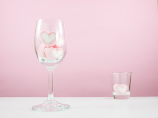 The lovely pink heart marshmallows in wine glass and shot glass on white table for Valentine's day.
