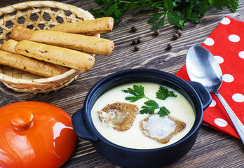 Cheese soup with croutons in pot on a wooden background