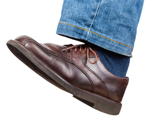 left leg in jeans and brown shoe takes a step