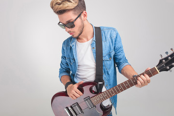 blonde man in studio wearing glasses while holding a guitar