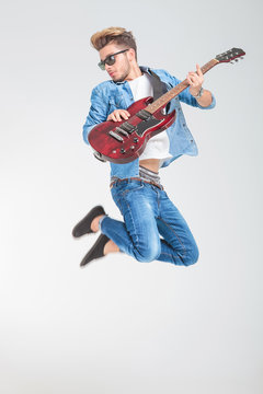 male artist jumping in studio while playing guitar