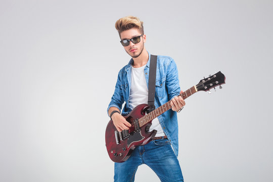 artist playing guitar in studio background while wearing sunglas