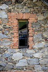 sauberes Fenster, uralte Hauswand aus Granit und Ziegeln mit kleinem spiegelndem Fenster