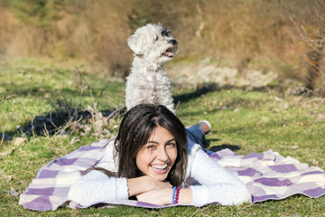 smiling woman laying on a meadow with her small poodle dog