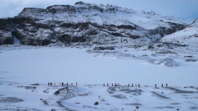 Large group of people walking under high snowy mountains, extreme traveling expedition to glacier Solheimajokull, Iceland. Full HD Video 1920x1080