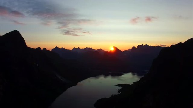 Aerial footage of midnight sun slowly hiding behind mountain peak on Lofoten islands in Norway. Aerial 4k Ultra HD.