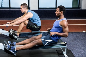 Muscular men using rowing machine