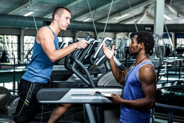 Muscular man using elliptical machine with trainer 