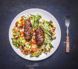 grilled kebab on skewer with a salad of various vegetables on a white plate with a fork on wooden rustic background top view close up