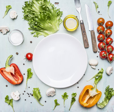 variety of vegetables laid out around a white plate with oilknife and fork on wooden rustic background top view close up