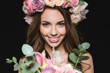 Happy charming young female in roses wreath holding beautiful bouquet