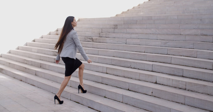 Serious young business woman in high heel shoes walking up long flight of marble stairs outdoors